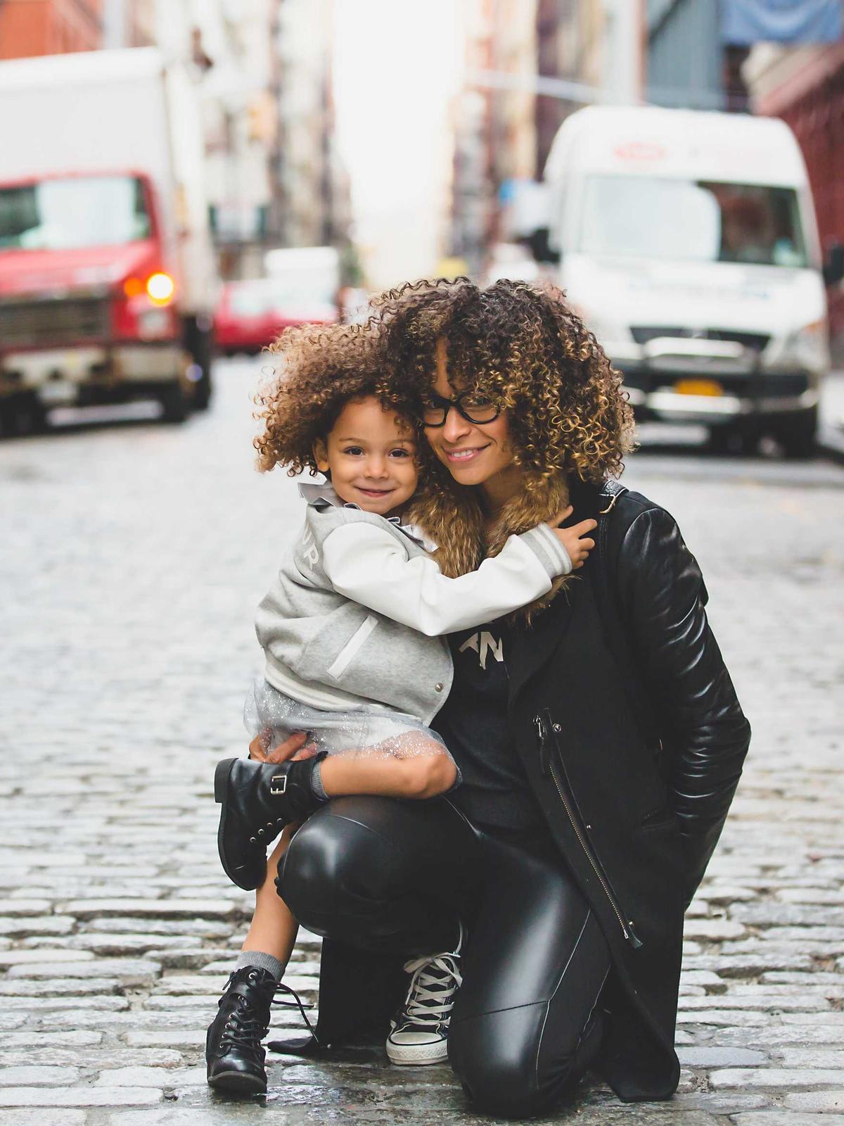 A mother kneeling to hold her young child close on a city street